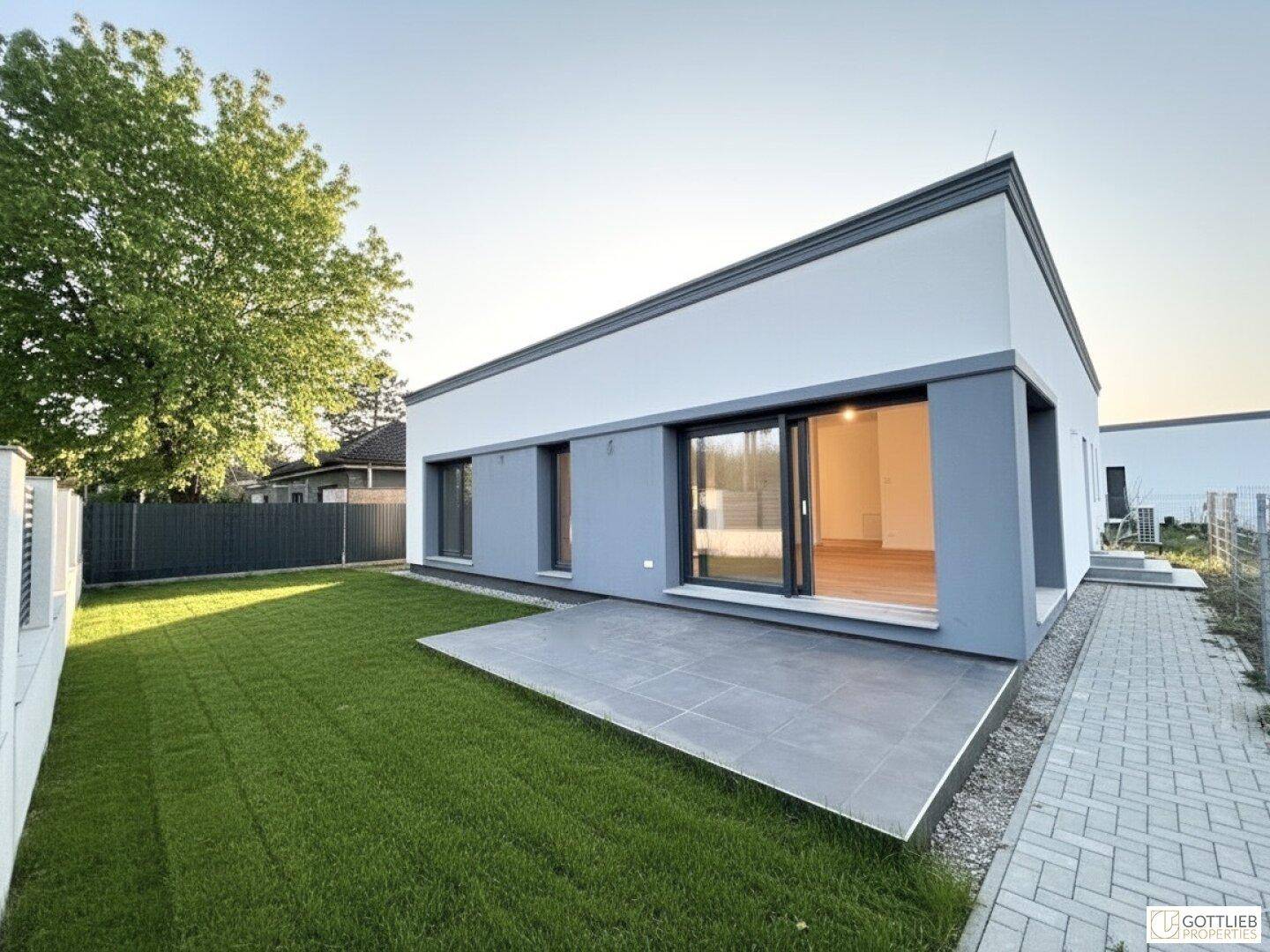 Ansicht des modernen Hauses mit großer Terrasse, gepflegtem Rasen und breiten Fensterfronten.