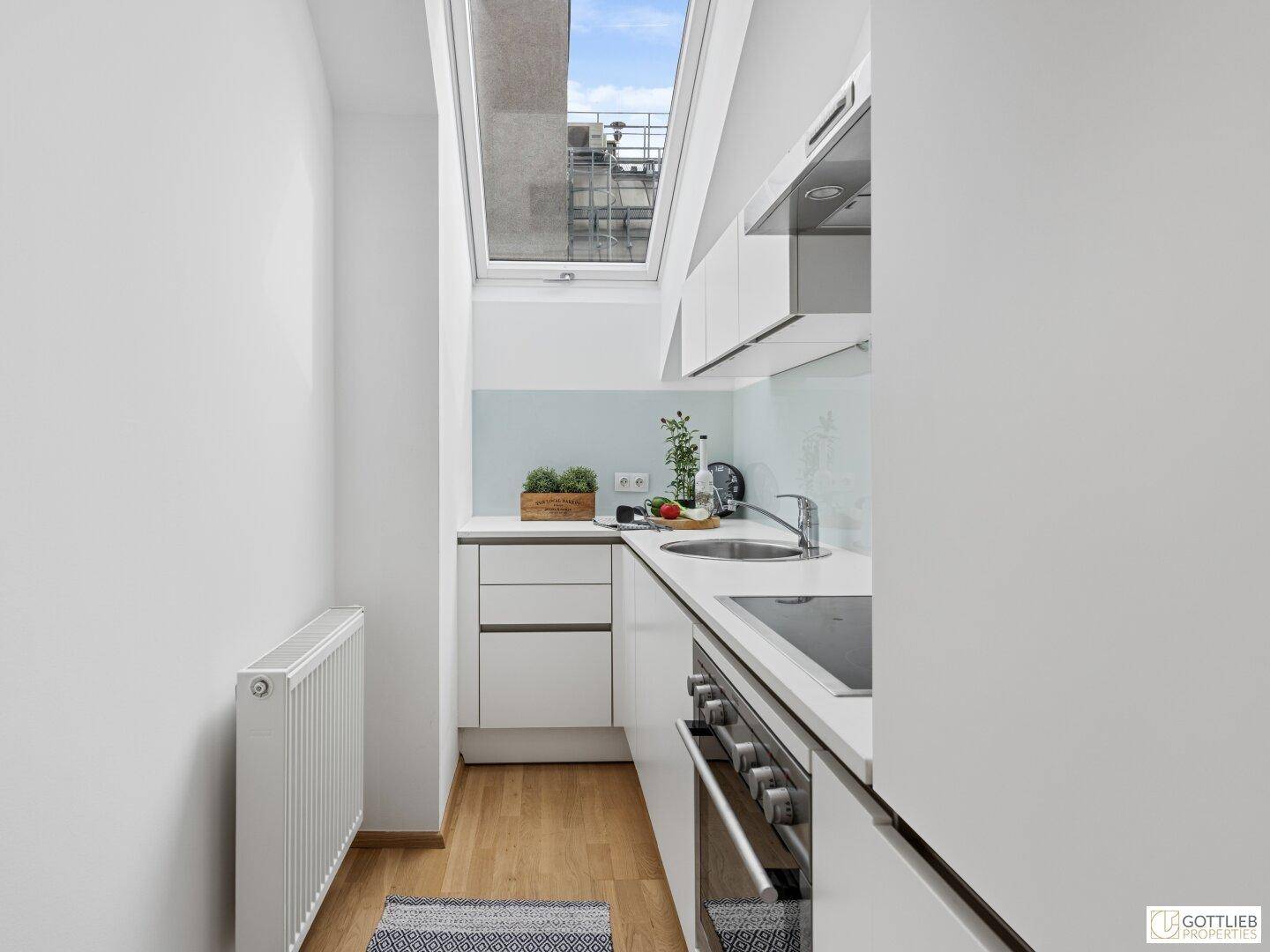 Moderne, kompakte Küche mit weißen Schränken, Einbaugeräten und einem praktischen Dachfenster.