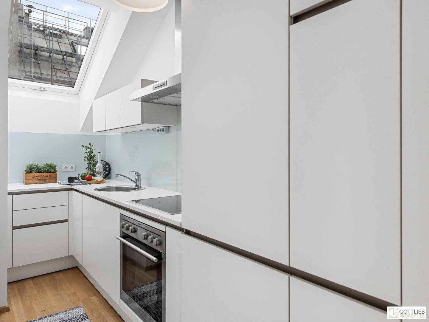 Helle Einbauküche mit weißen Fronten, integriertem Kühlschrank und viel natürlichem Licht durch das Dachfenster.