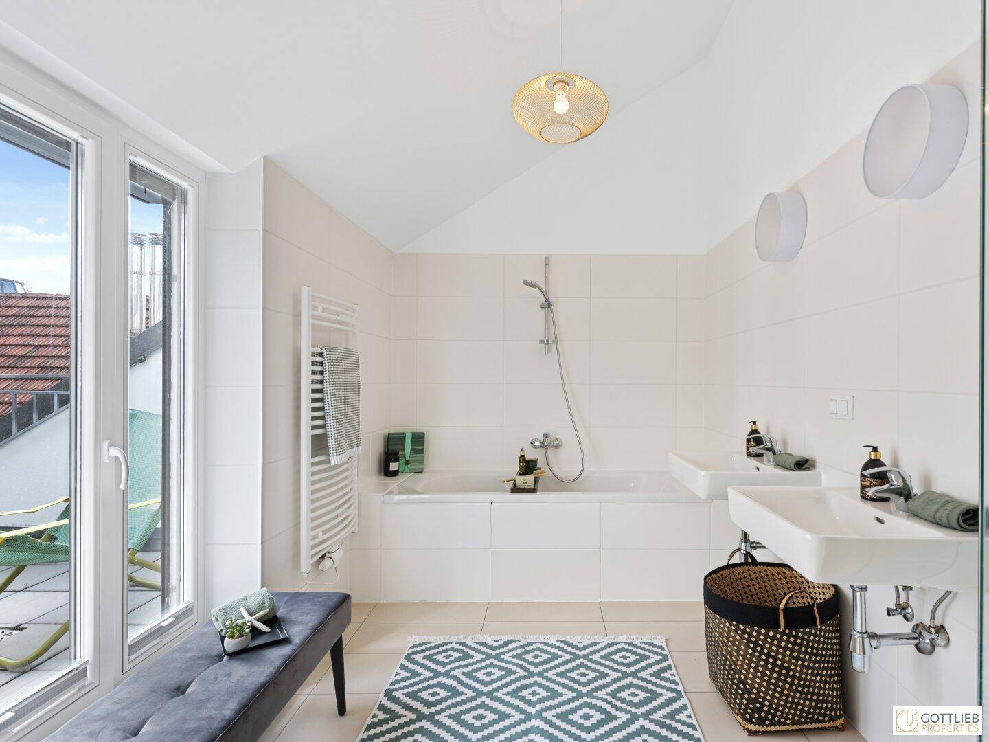 Geräumiges Badezimmer mit Badewanne, zwei Waschbecken, Handtuchheizkörper und großen Fenstern.