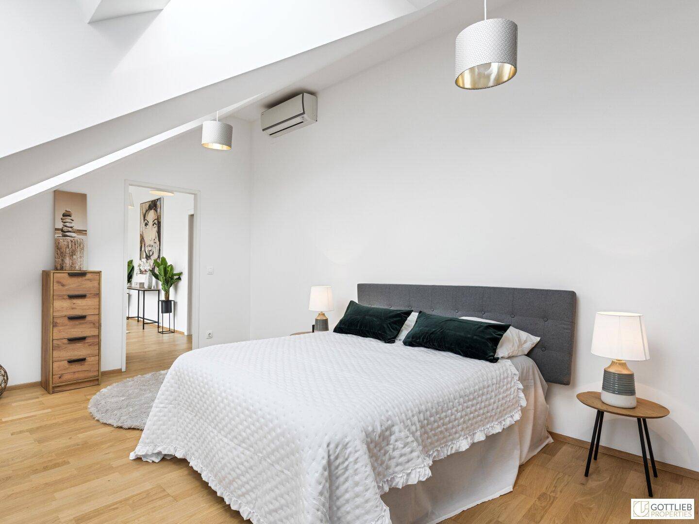 Helles Schlafzimmer mit Holzboden, schräger Decke und Klimaanlage, bietet Zugang zum Flur.