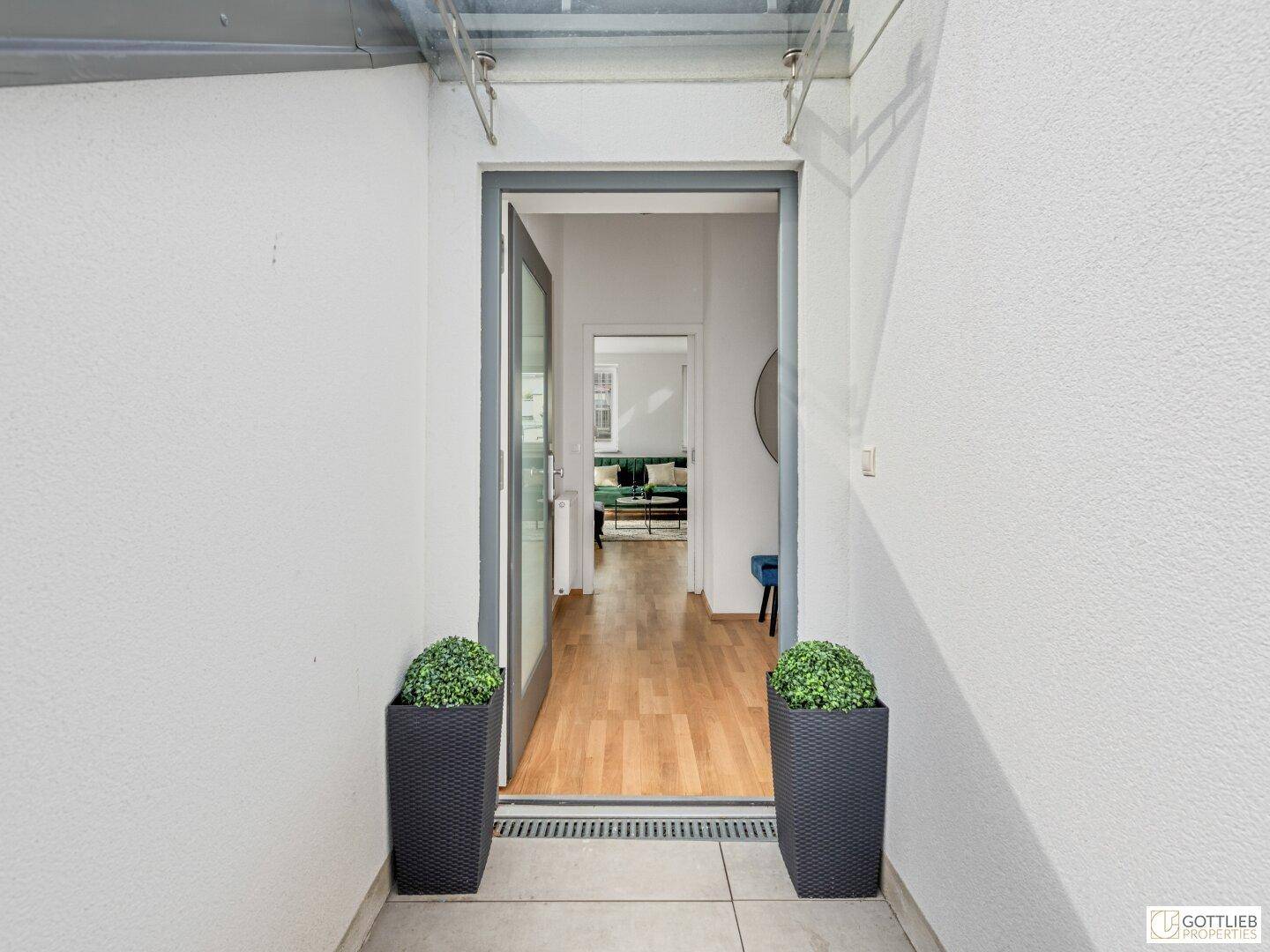 Moderner Hauseingang mit Glasfront, der in einen hellen Flur mit Holzboden führt.