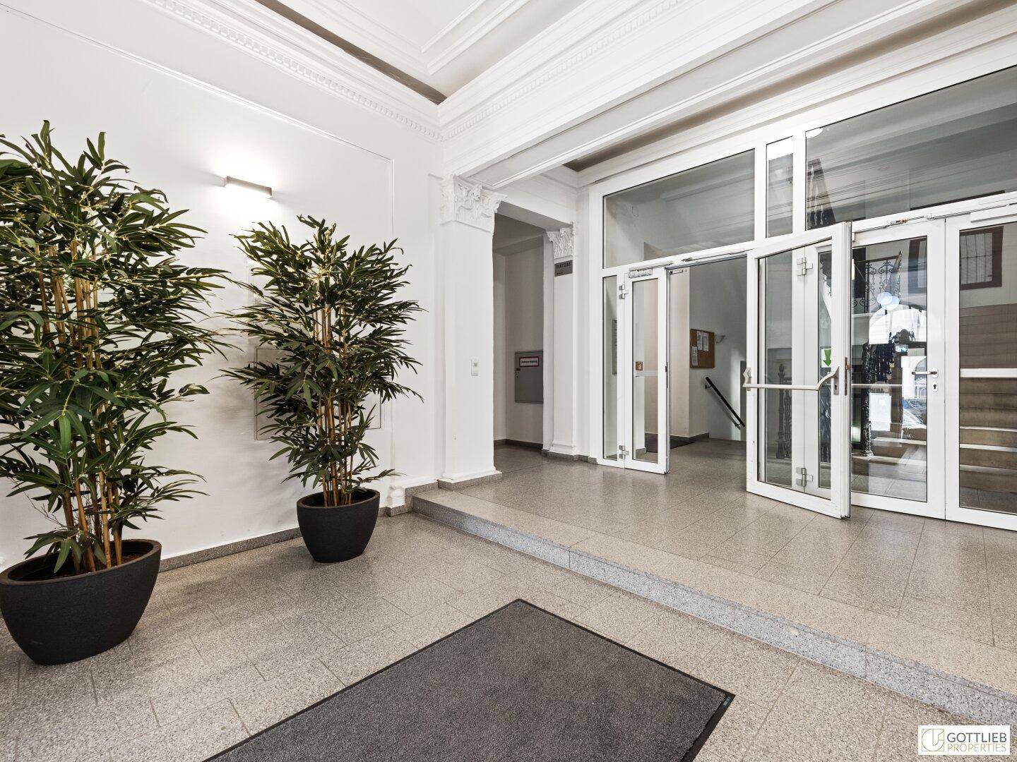 Repräsentativer Eingangsbereich eines Gebäudes mit hohen Decken, großen Glasfronten und Pflanzen.