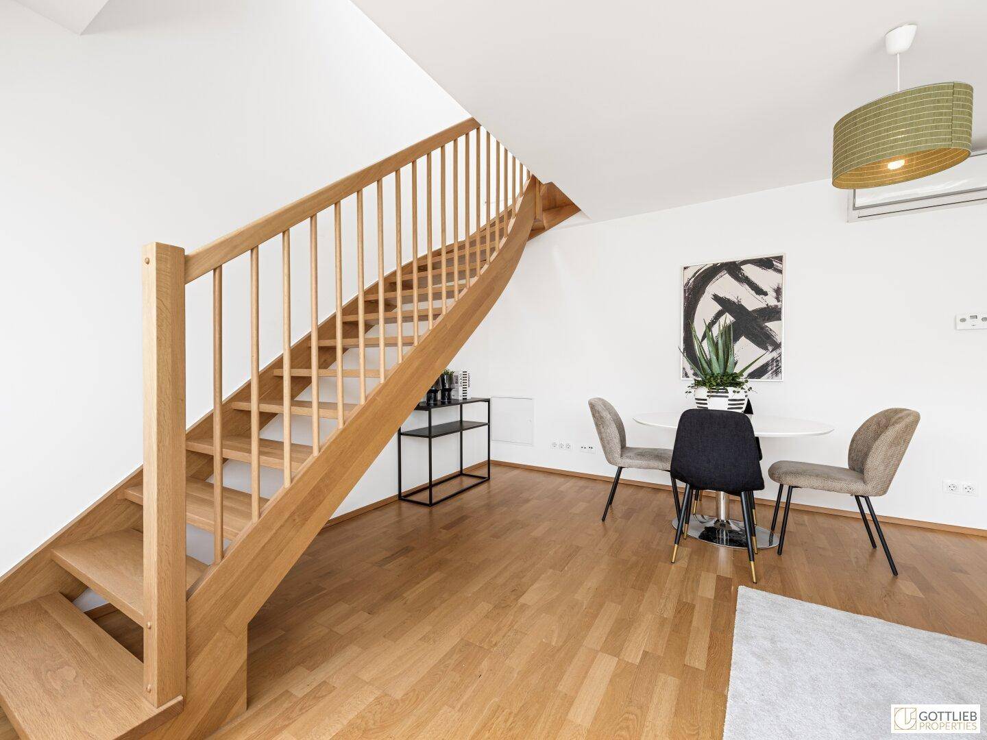 Elegante Holztreppe führt in die obere Etage, mit Essbereich und moderner Kunst im Hintergrund.