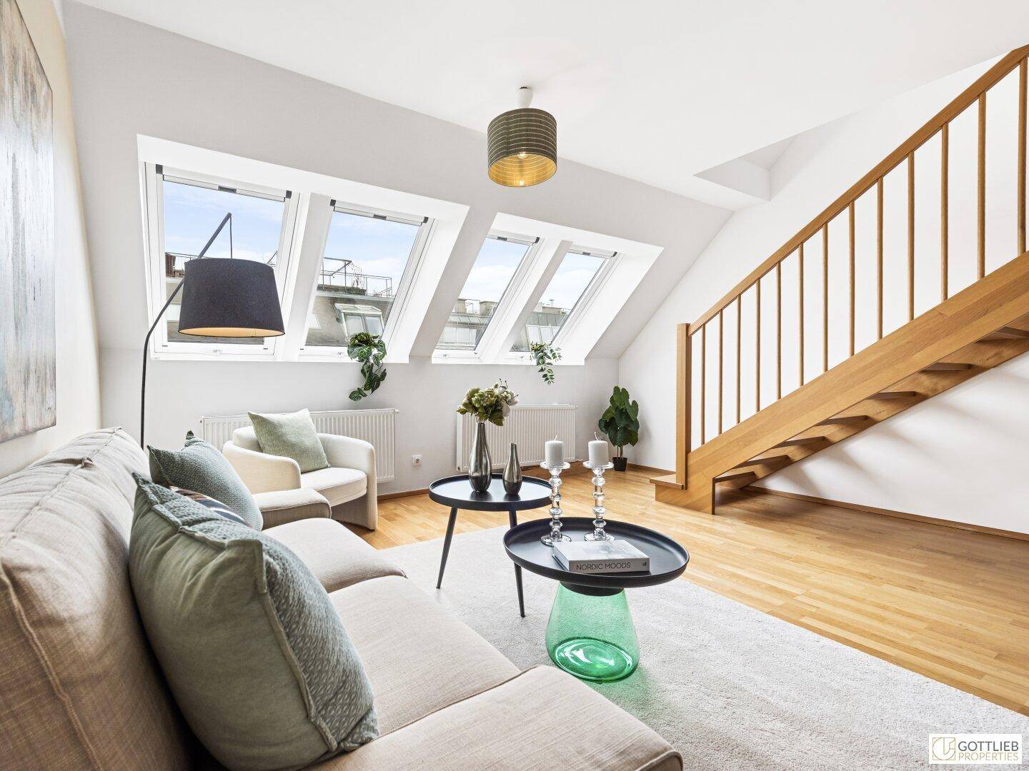 Heller Wohnbereich mit bequemer Couch, Dachfenstern und Zugang zur oberen Etage über die Holztreppe.