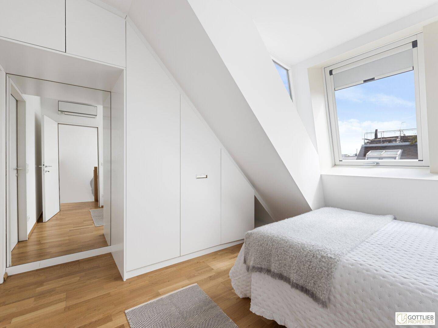 Schlafzimmer mit integrierten Kleiderschränken, Dachschräge und einem hellen Dachfenster für Tageslicht.