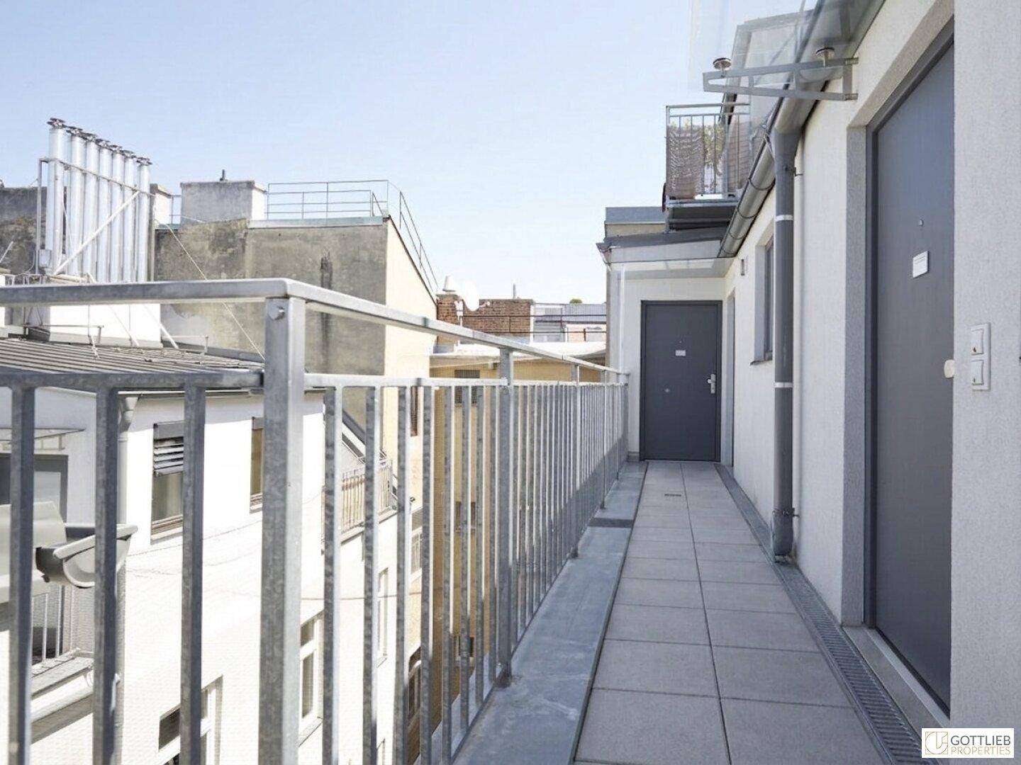 Langer Außenbalkon mit Metallgeländer und Fliesenboden, der Zugang zu den Wohneinheiten bietet.