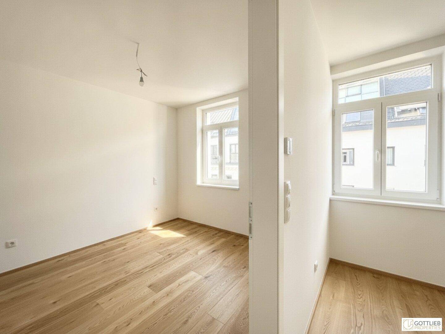 Heller Raum mit Holzboden und weißen Wänden, durchflutet von natürlichem Sonnenlicht.