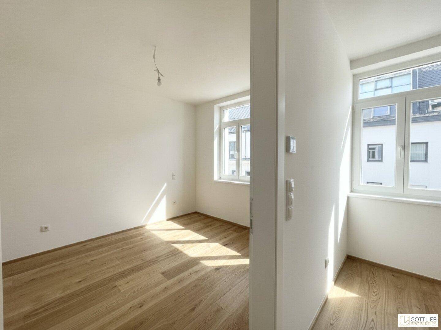 Heller Raum mit Holzboden und weißen Wänden, durchflutet von natürlichem Sonnenlicht.