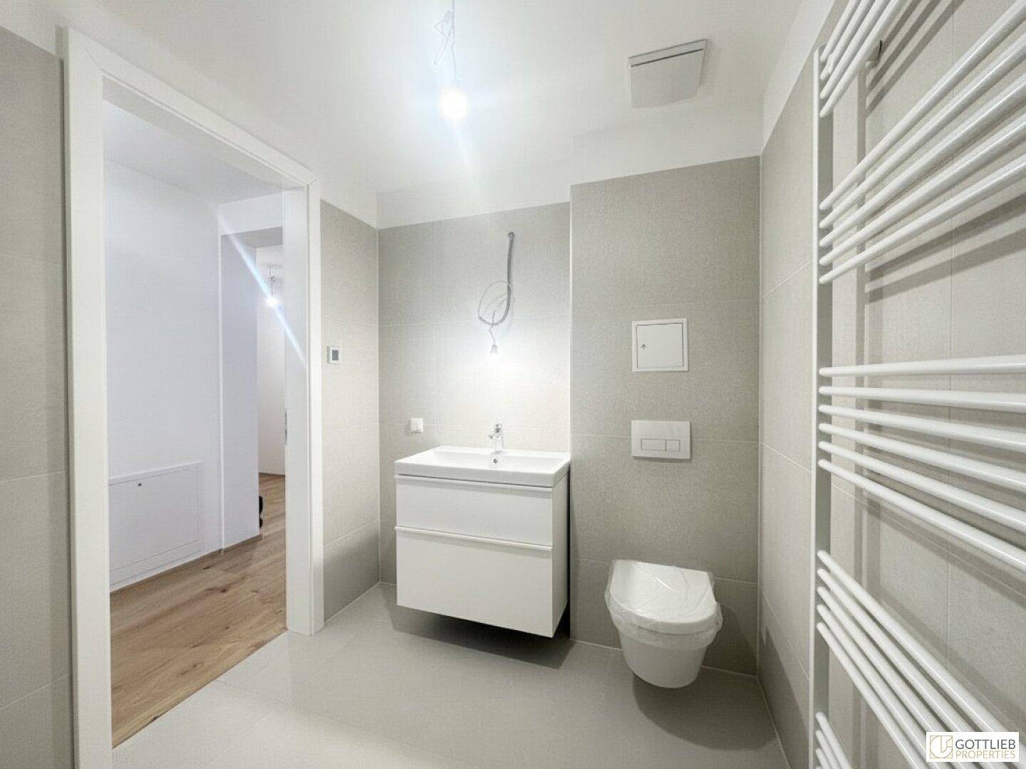 Modernes Badezimmer mit Wand-WC, Einzelwaschbecken und beheiztem Handtuchhalter.