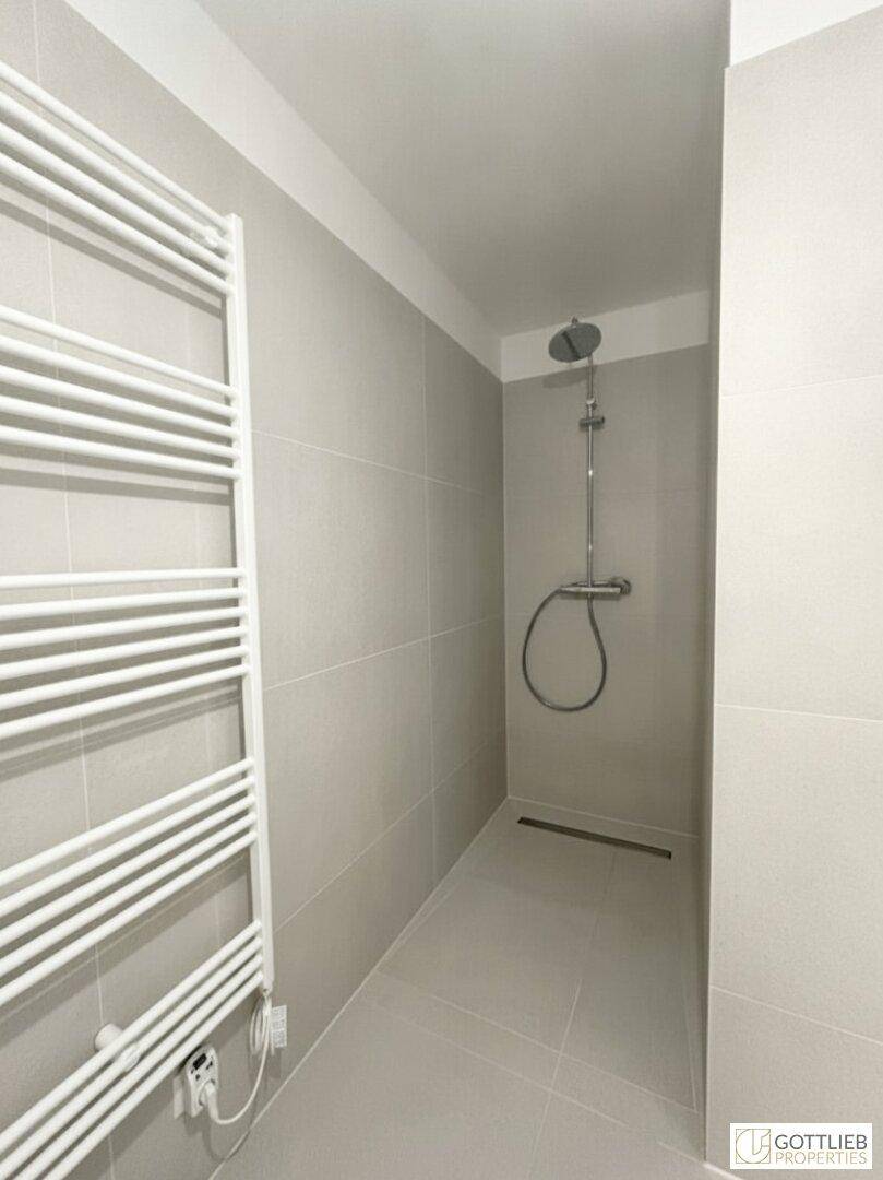 Moderne Dusche mit grauen Fliesen und praktischem beheiztem Handtuchhalter.