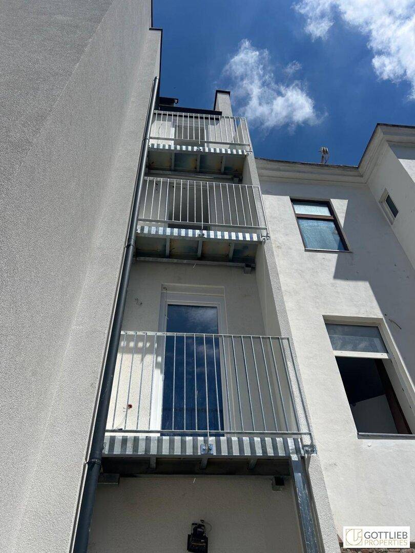 Gebäudefassade mit mehreren Balkonen und einer externen Fluchttreppe unter blauem Himmel.