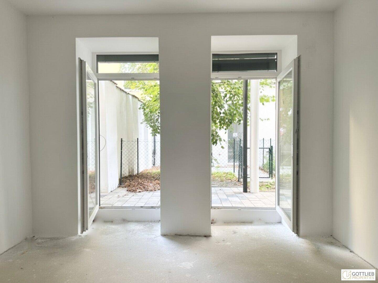 Heller, leerer Raum mit großen Fenstertüren, die Zugang zu einem Außenbereich bieten.