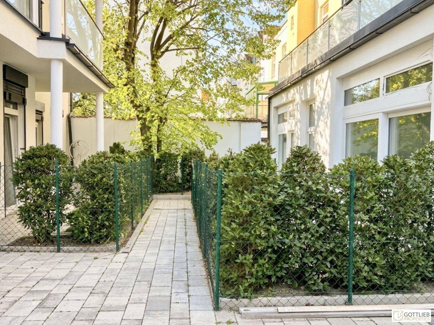 Gepflasterter Außenbereich mit grünen Hecken und Bäumen, der einen ruhigen Innenhof bildet.