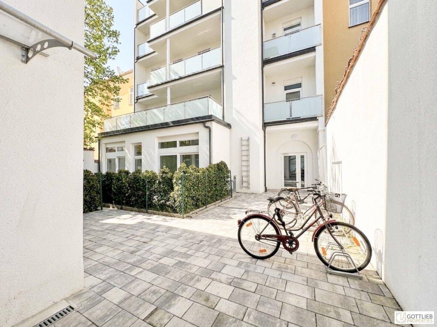 Moderne Gebäudefassade mit mehreren Balkonen und einem gepflasterten Außenbereich mit Fahrradabstellplatz.
