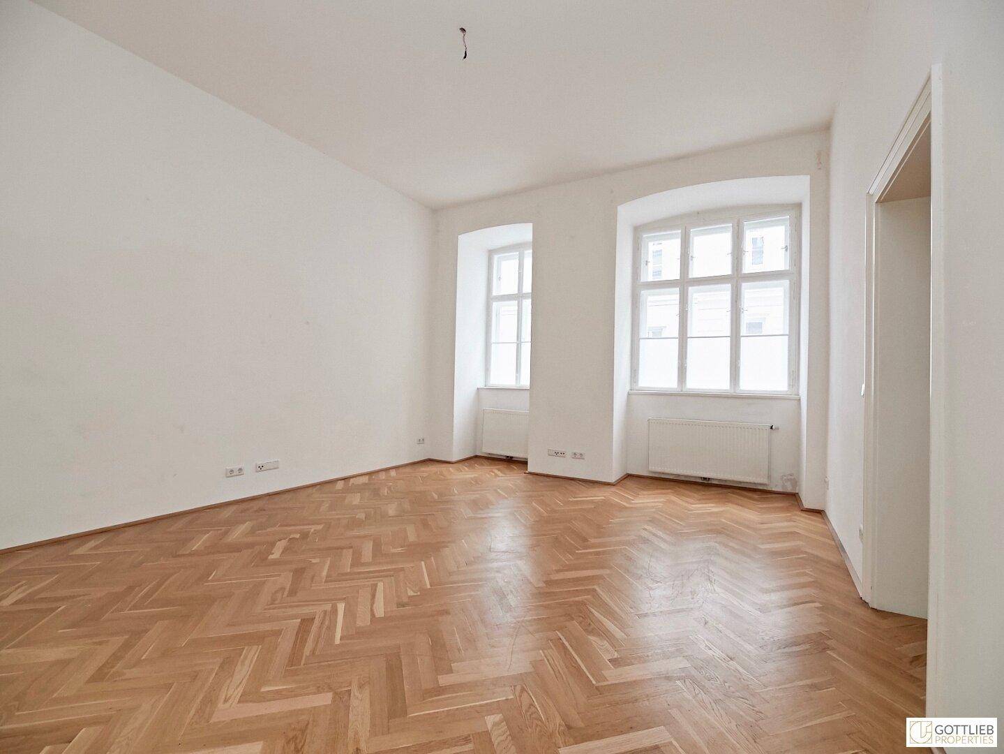 Heller Wohnraum mit klassischem Fischgrätparkett und großen Fenstern, die für viel Tageslicht sorgen.