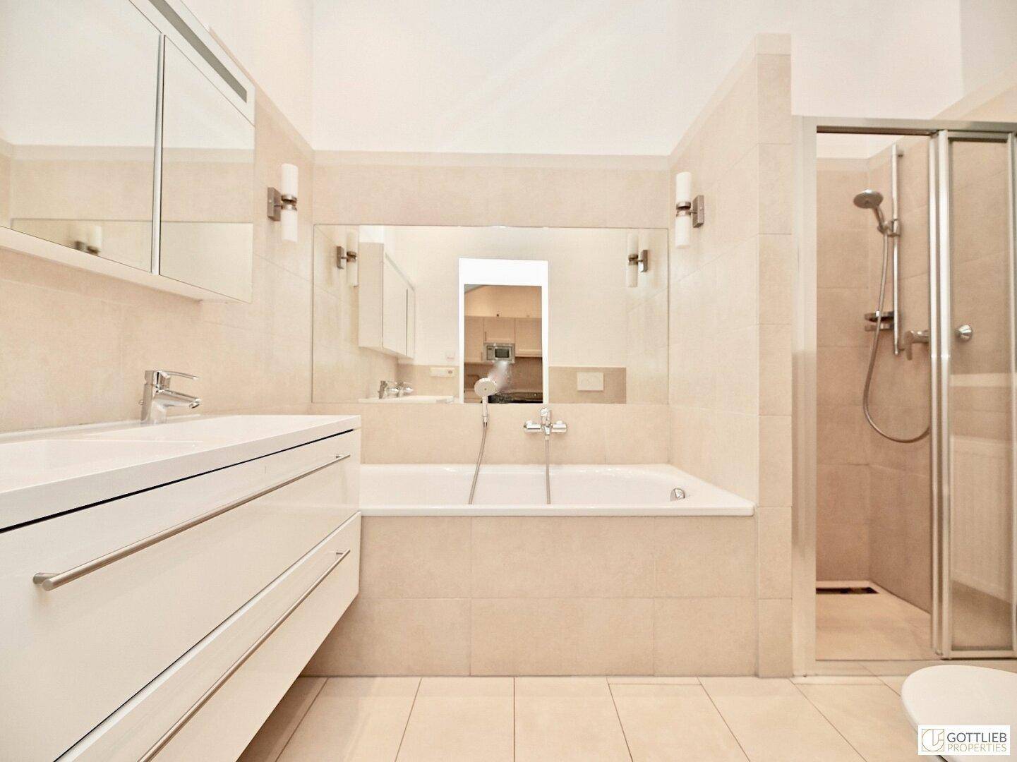 Helles Badezimmer mit Badewanne, Duschkabine und modernem Waschtisch, in beigen Fliesen gehalten.