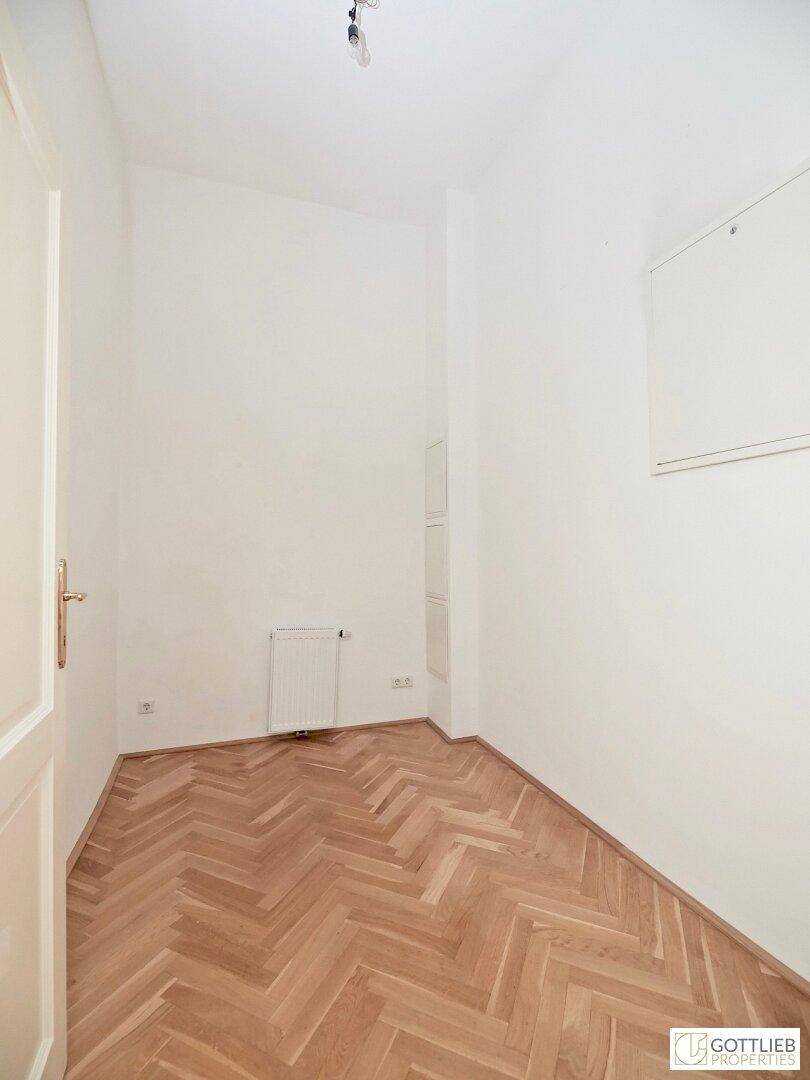 Kleiner, heller Raum mit Fischgrätparkett und weiß gestrichenen Wänden, ideal als Abstellraum.