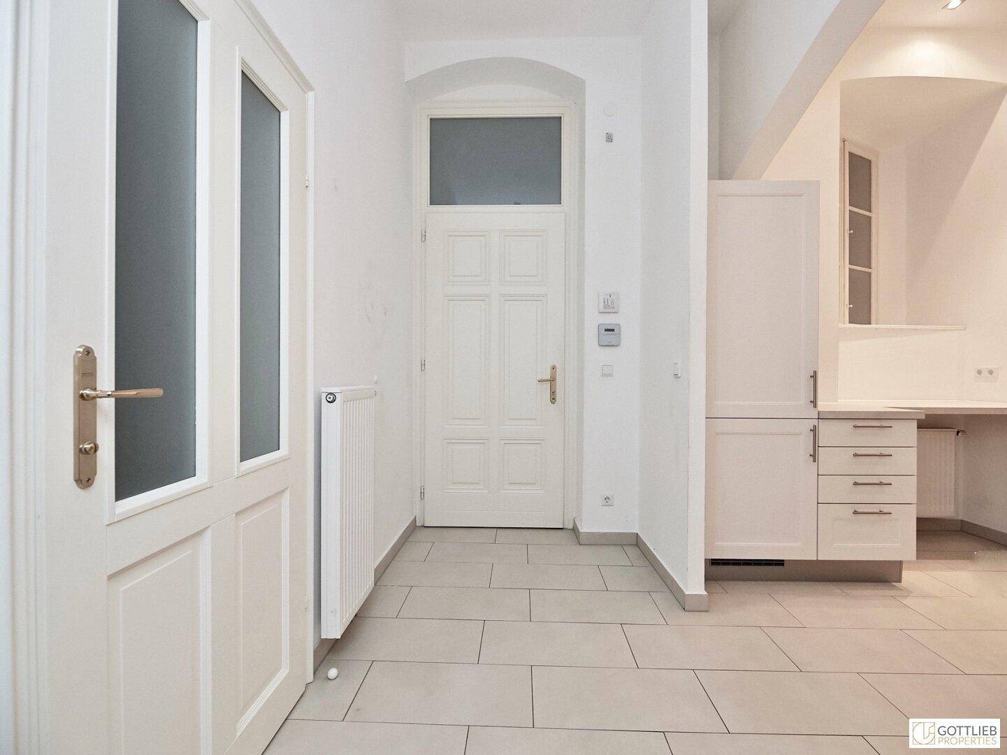Heller Eingangsbereich mit Fliesenboden, einer weißen Eingangstür und einem Einbauschrank.