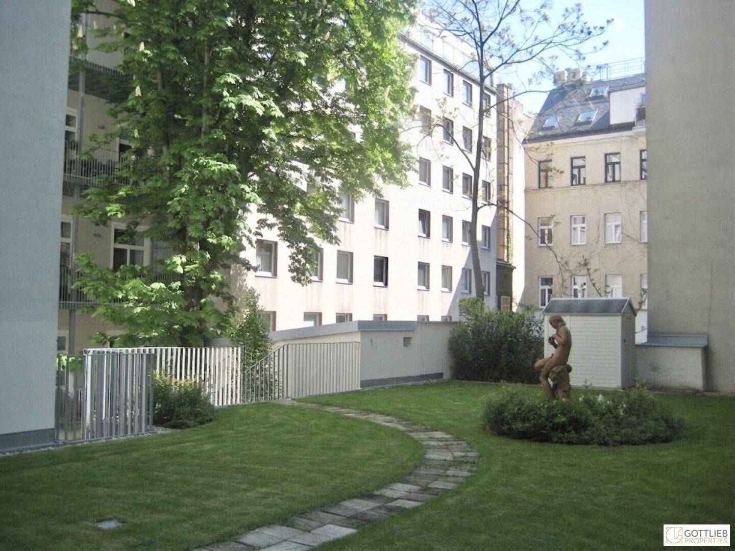 Gepflegter Innenhofgarten mit Rasenfläche, Steinpfad und einer Statue, umgeben von Gebäuden.