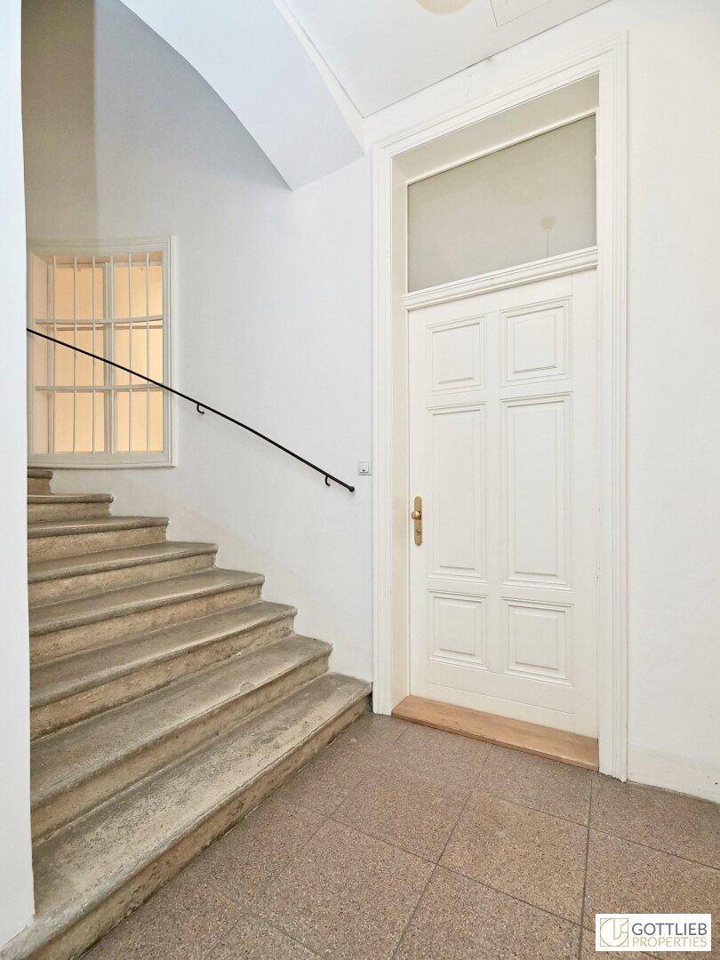 Treppenhaus mit Steinstufen, einem schlichten Handlauf und einer großen Eingangstür.