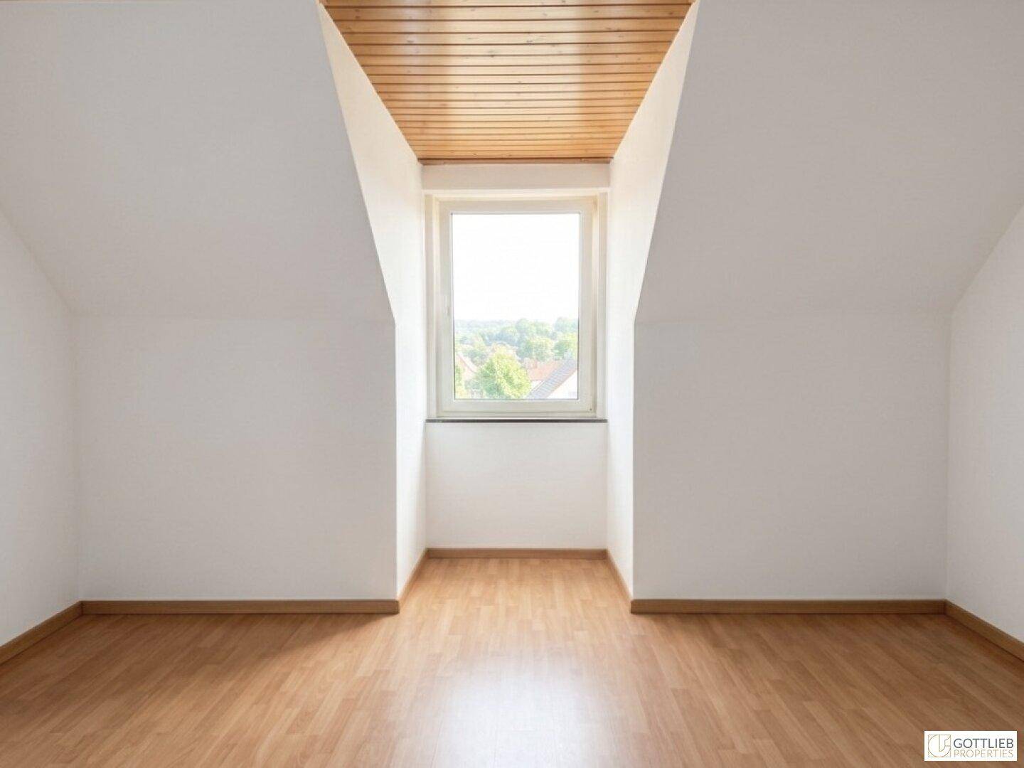 Leerer Raum im Dachgeschoss mit Holzbalkendecke, Laminatboden und Fenster mit Ausblick.