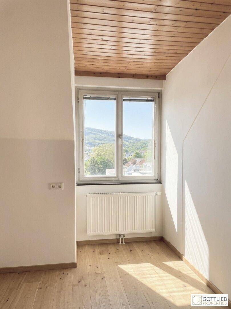 Heller Raum im Dachgeschoss mit Holzdecke, Heizkörper und Fenster mit Blick ins Grüne.