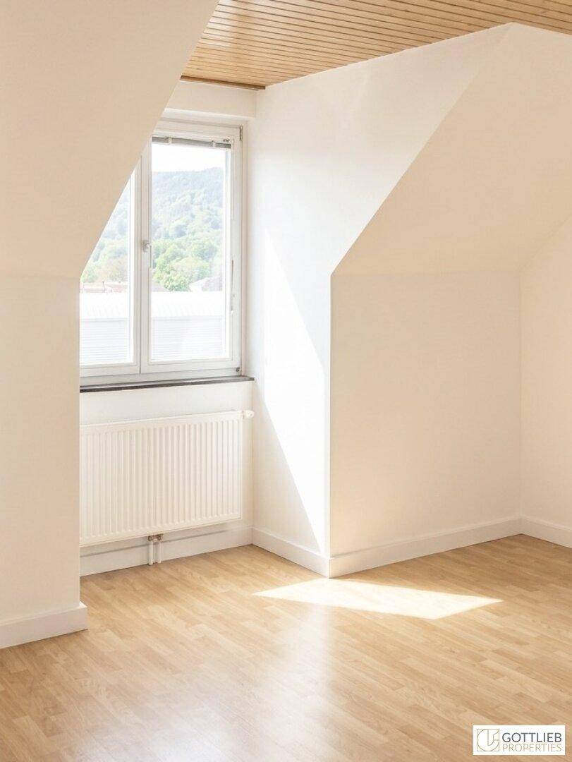 Sonnendurchfluteter Dachgeschossraum mit Holzdecke, Laminatboden und schrägen Wänden.