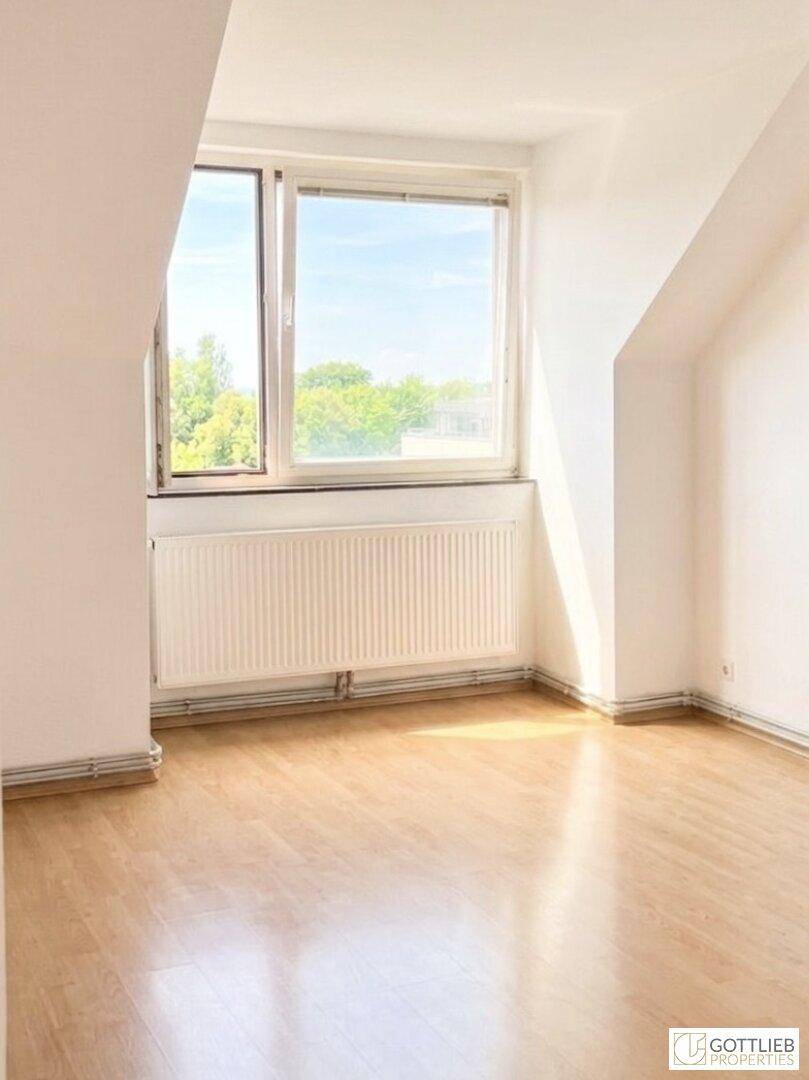 Geräumiger Dachgeschossraum mit Holzdecke, Laminatboden und viel Tageslicht durch das Fenster.
