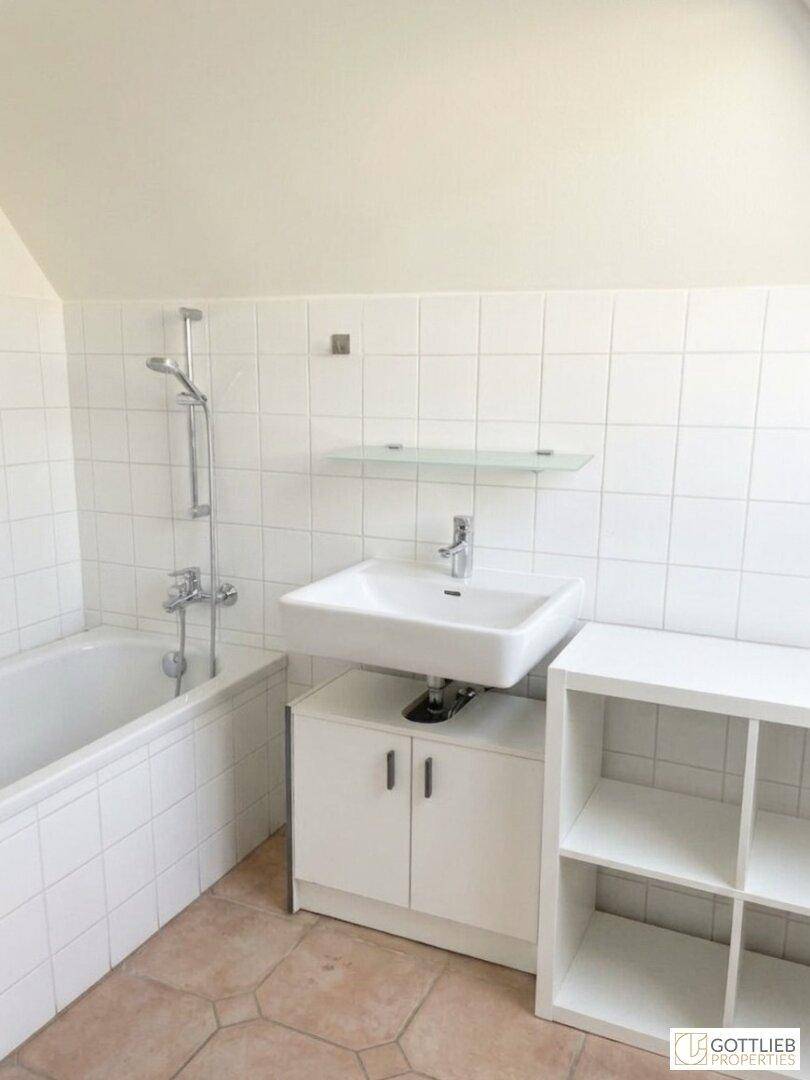 Helles Badezimmer mit Badewanne, Waschbecken und weißen Fliesen im Dachgeschoss.