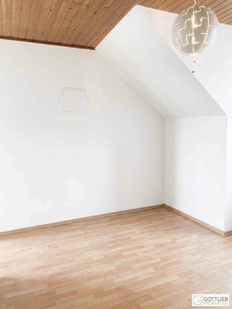 Leerer Dachgeschossraum mit Holzdecke und Laminatboden, bereit zur individuellen Gestaltung.