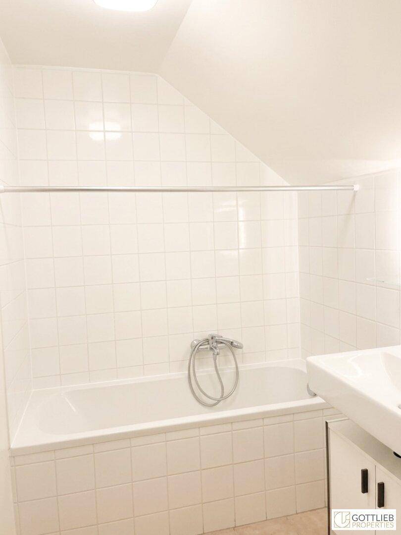 Badezimmer mit Badewanne und weißen Wandfliesen unter einer Dachschräge.