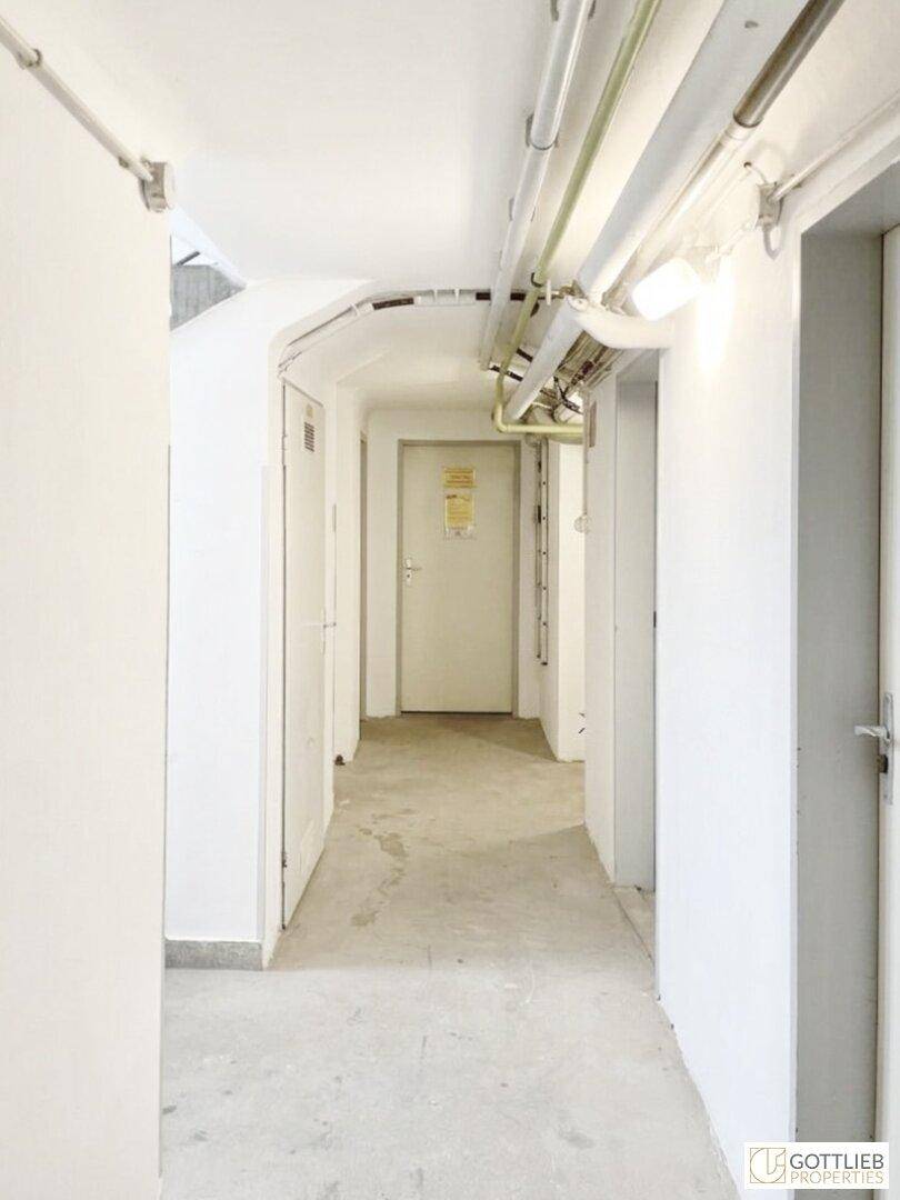 Schmaler Flur im Kellerbereich mit sichtbaren Leitungen und Betonboden.