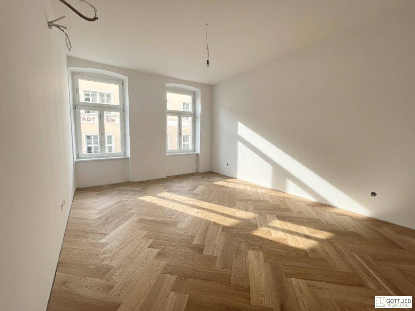 Geräumiger, heller Raum mit Fischgrätparkett und großen Fenstern, bereit für die Einrichtung.