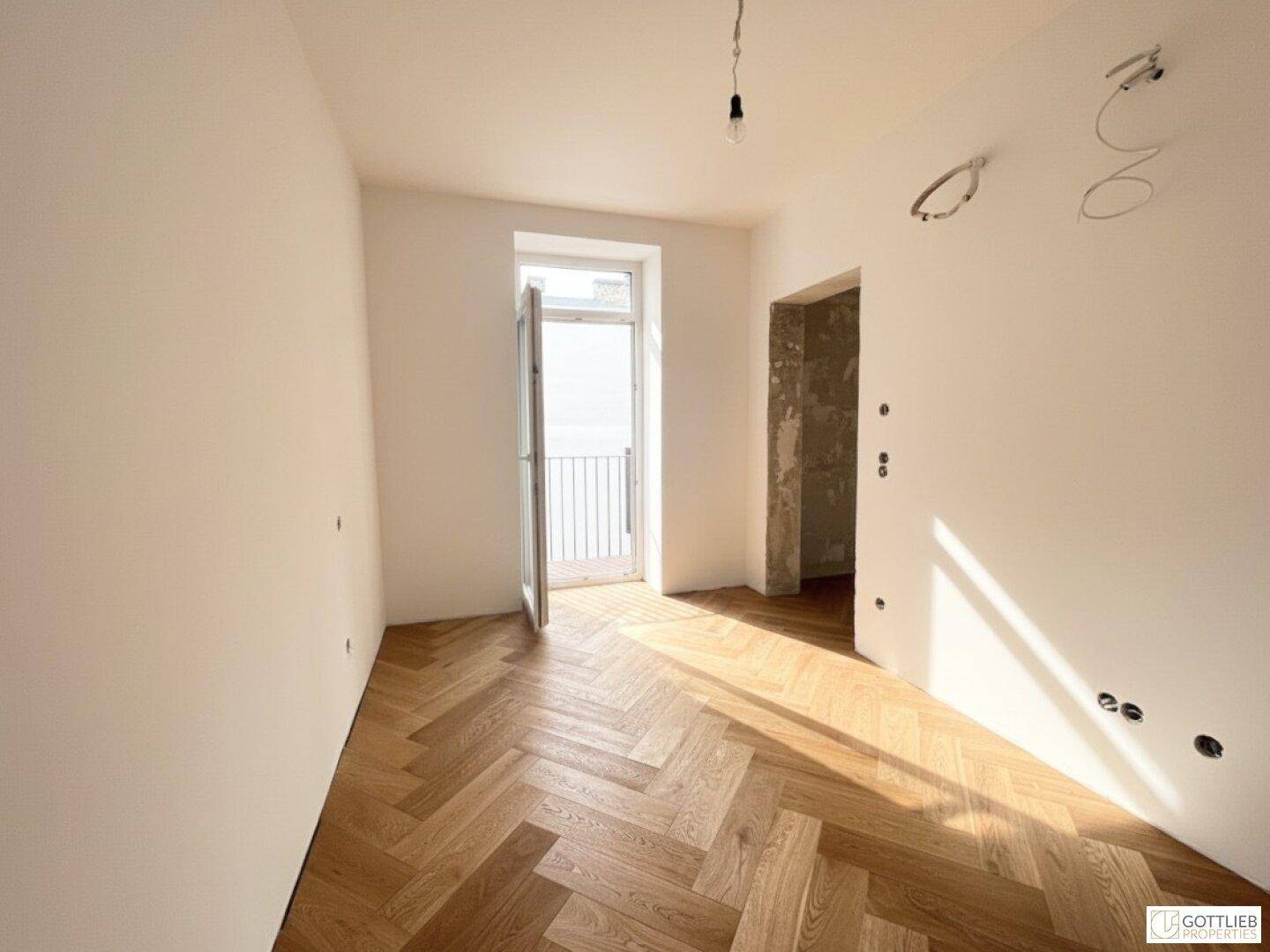 Heller Raum mit Fischgrätparkett und Zugang zu einem französischen Balkon, vielseitig nutzbar.