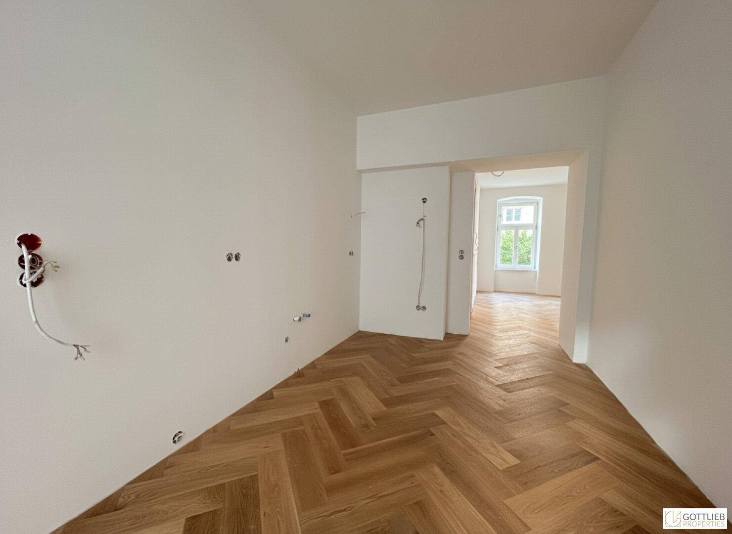 Heller Flur mit Fischgrätparkett und Durchgang zu einem weiteren Raum, noch im Ausbau.