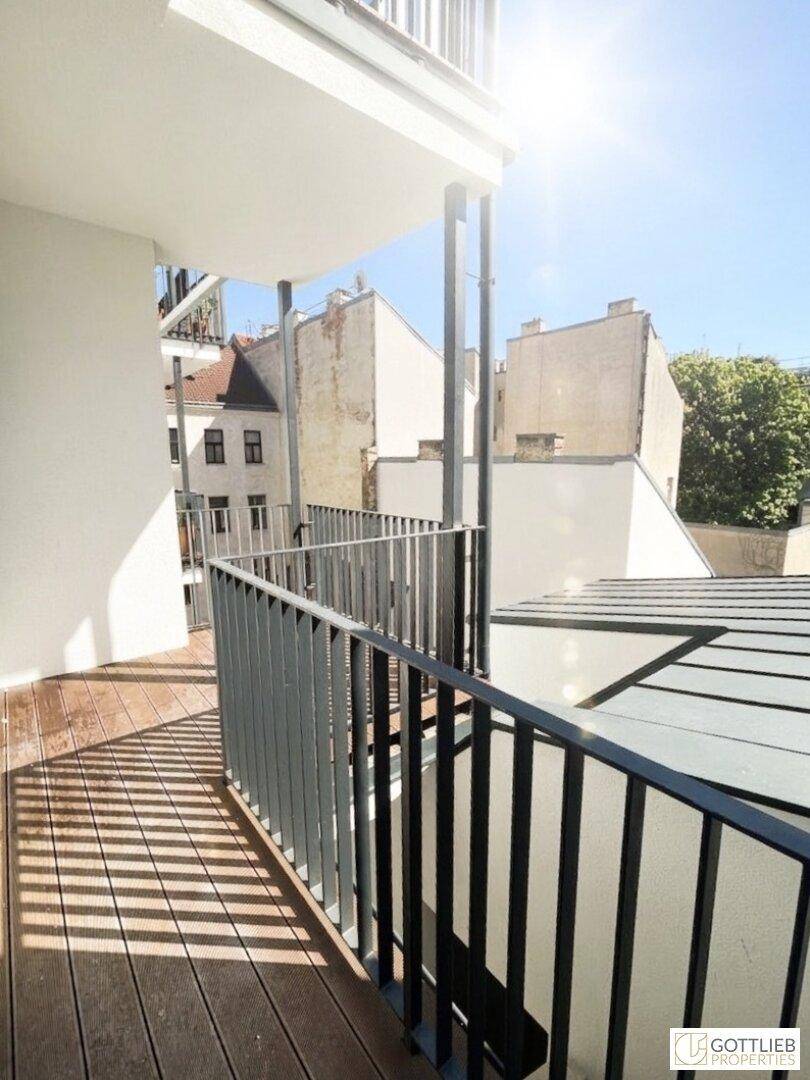 Langer Balkon mit Holzboden und Metallgeländer, bietet einen seitlichen Blick auf die Umgebung.