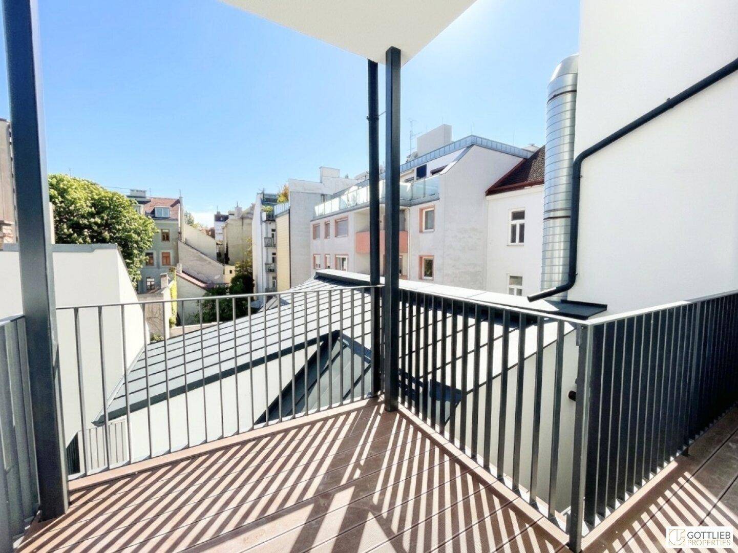 Heller Balkon mit Holzboden und Metallgeländer, bietet einen Blick auf die umliegenden Stadtgebäude.