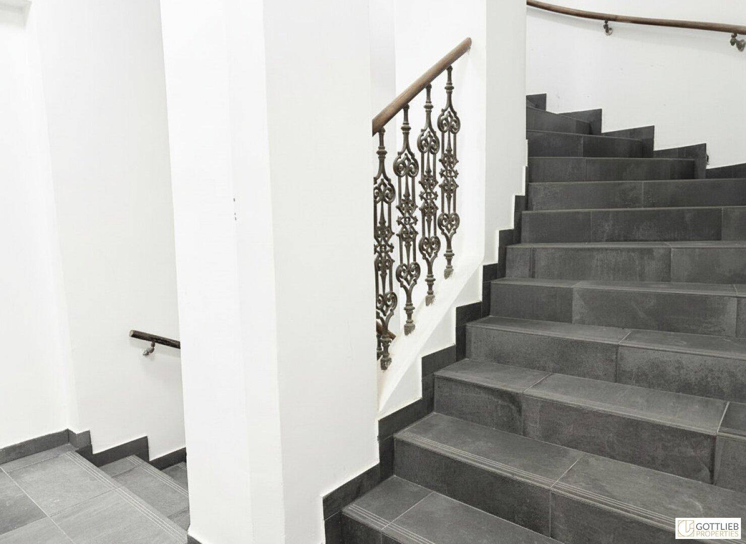 Elegantes Treppenhaus mit dunklen Steinstufen und kunstvollem schmiedeeisernem Geländer.