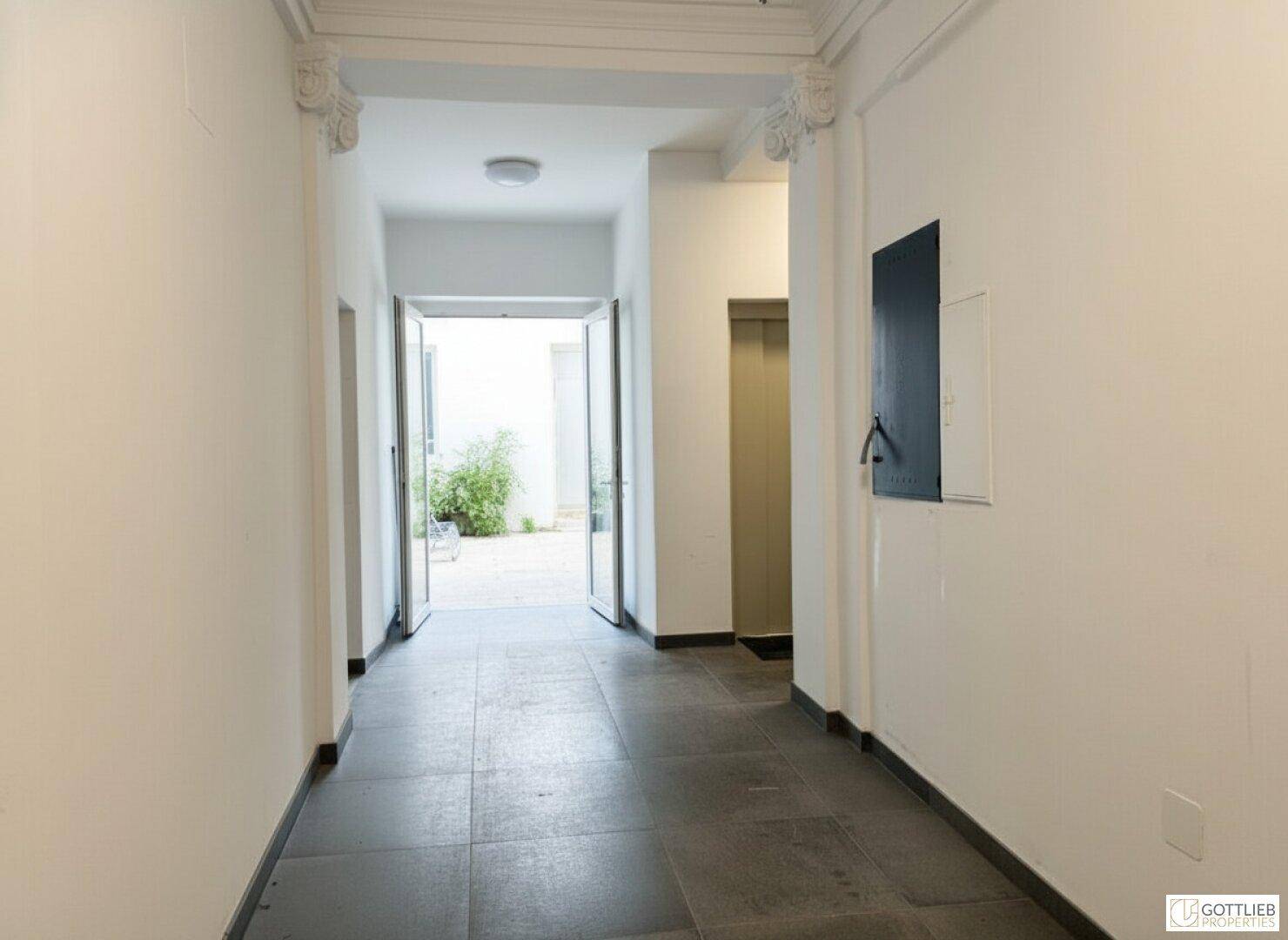 Freundlicher Eingangsbereich mit Fliesenboden und Blick in einen begrünten Innenhof.