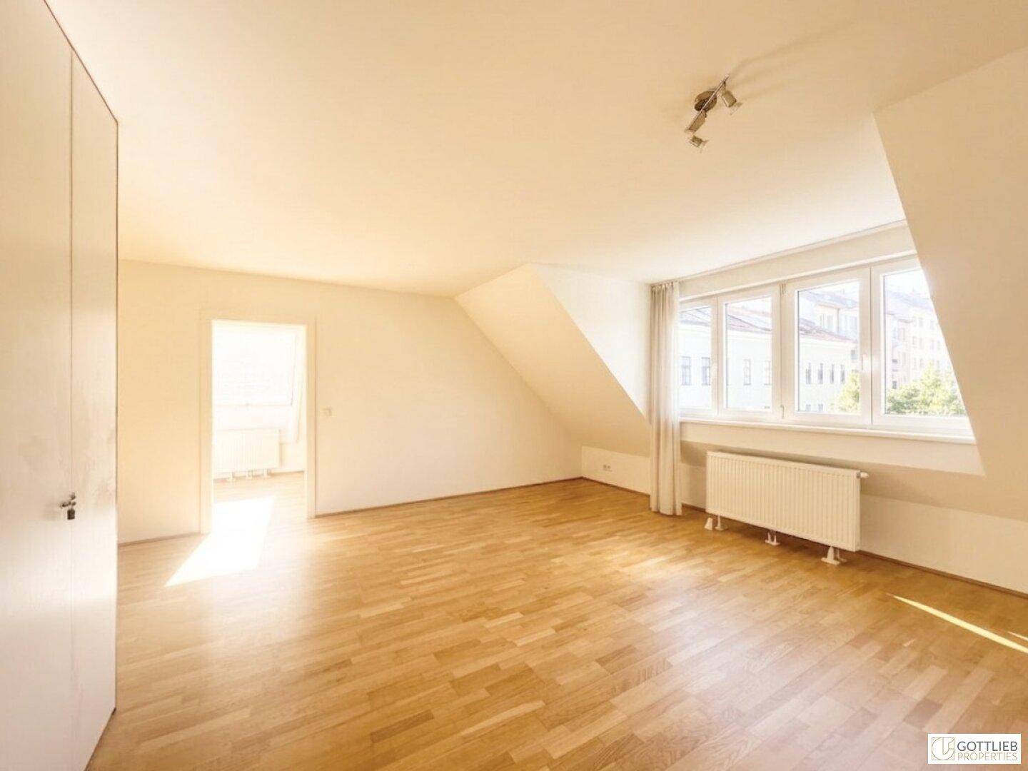 Helles Dachgeschosszimmer mit Holzboden, großen Fenstern und Blick auf die Stadt.