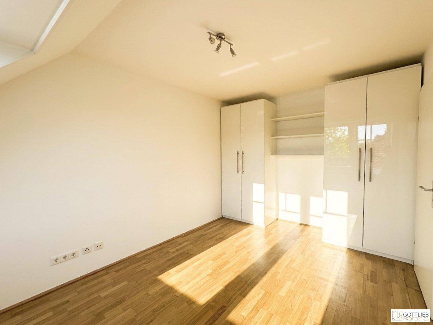Helles Schlafzimmer mit Holzboden und weißen Einbauschränken, mit viel Tageslicht.