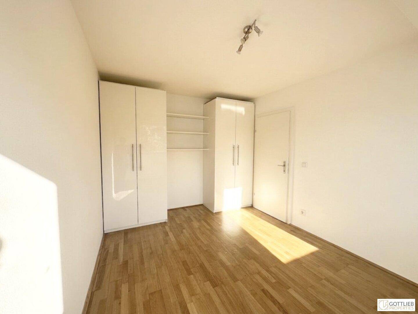 Helles Schlafzimmer mit Holzboden und weißen Einbauschränken, durchflutet von Sonnenlicht.