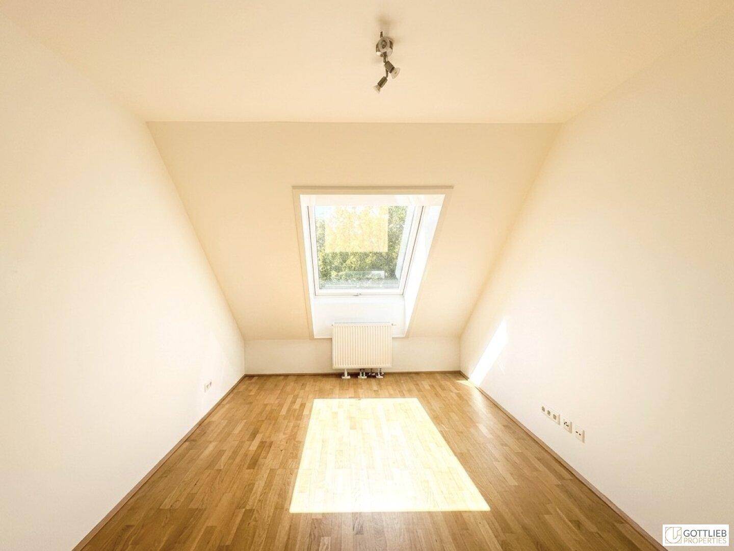 Dachgeschosszimmer mit Holzboden und großem Dachfenster, das viel Sonnenlicht hereinlässt.