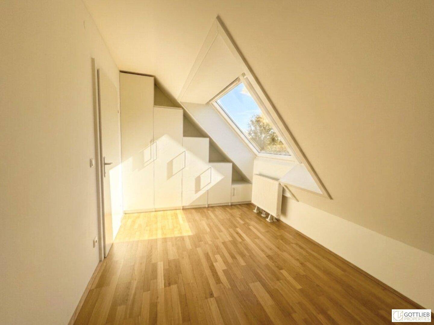 Dachgeschosszimmer mit Holzboden, Einbauschränken und einem schrägen Dachfenster.