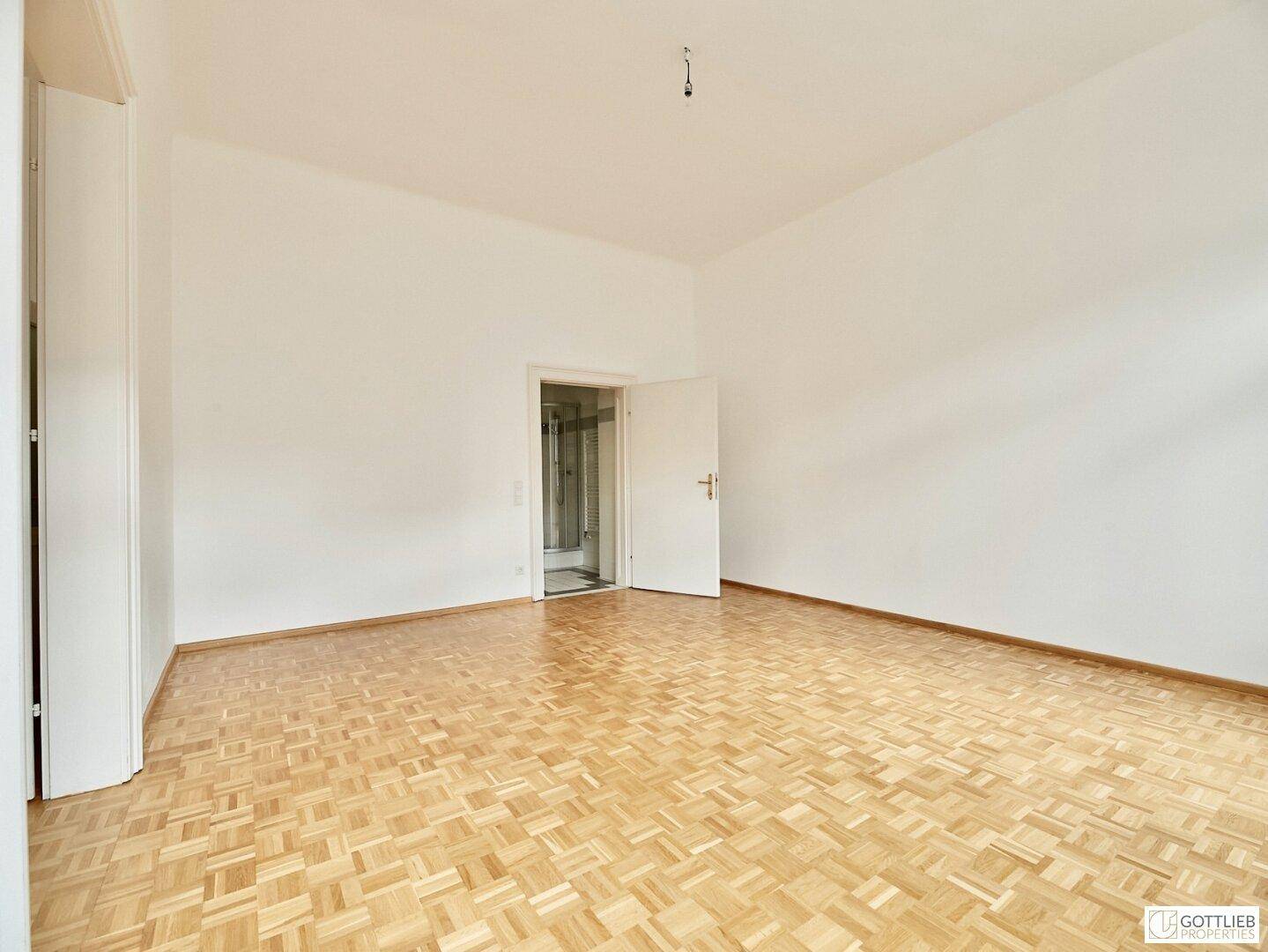 Leeres Zimmer mit Parkettboden und direktem Zugang zu einem Badezimmer mit Dusche.