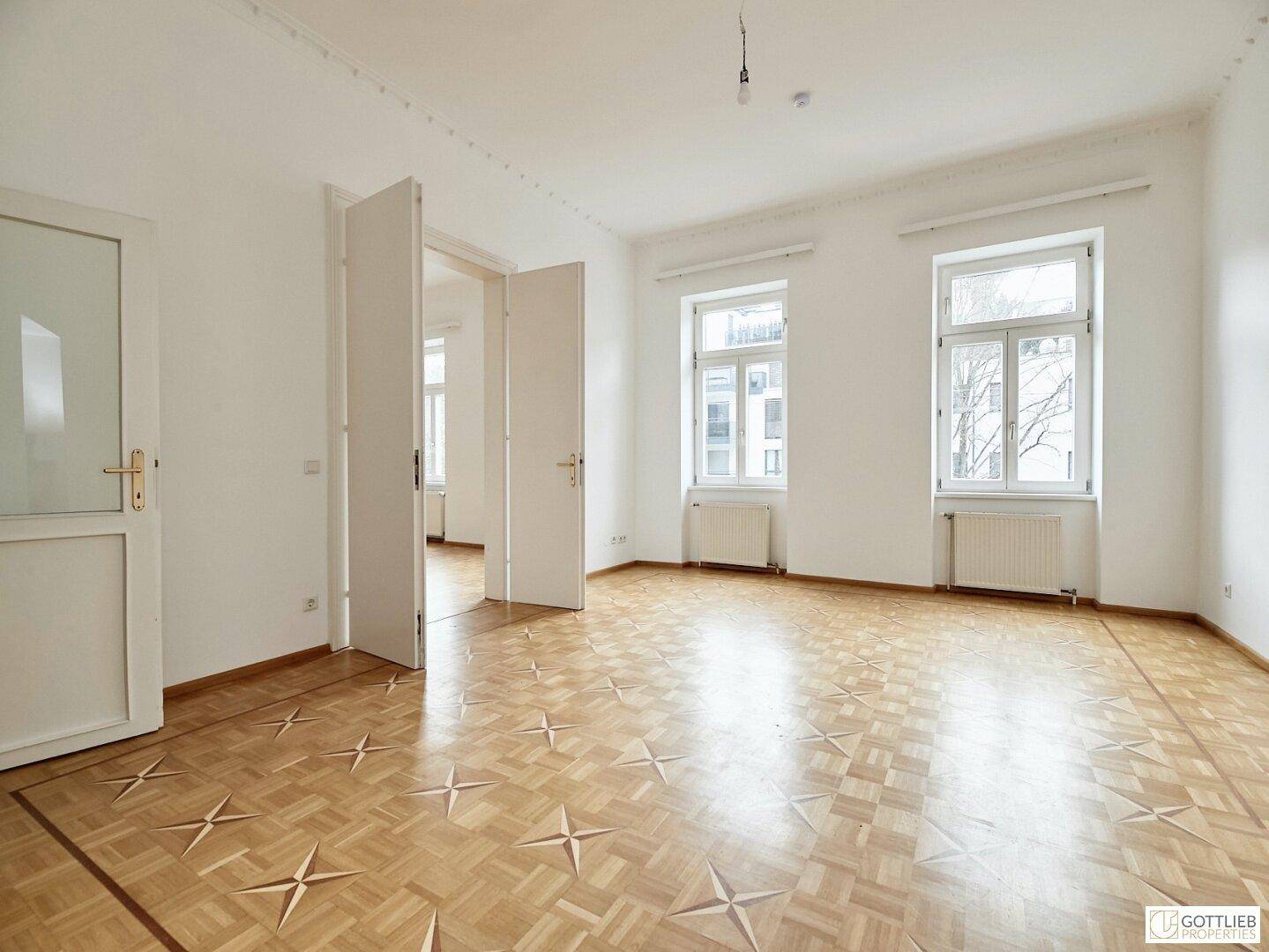 Helles, geräumiges Zimmer mit elegantem Parkettboden und hohen Decken, durch Doppeltüren verbunden.