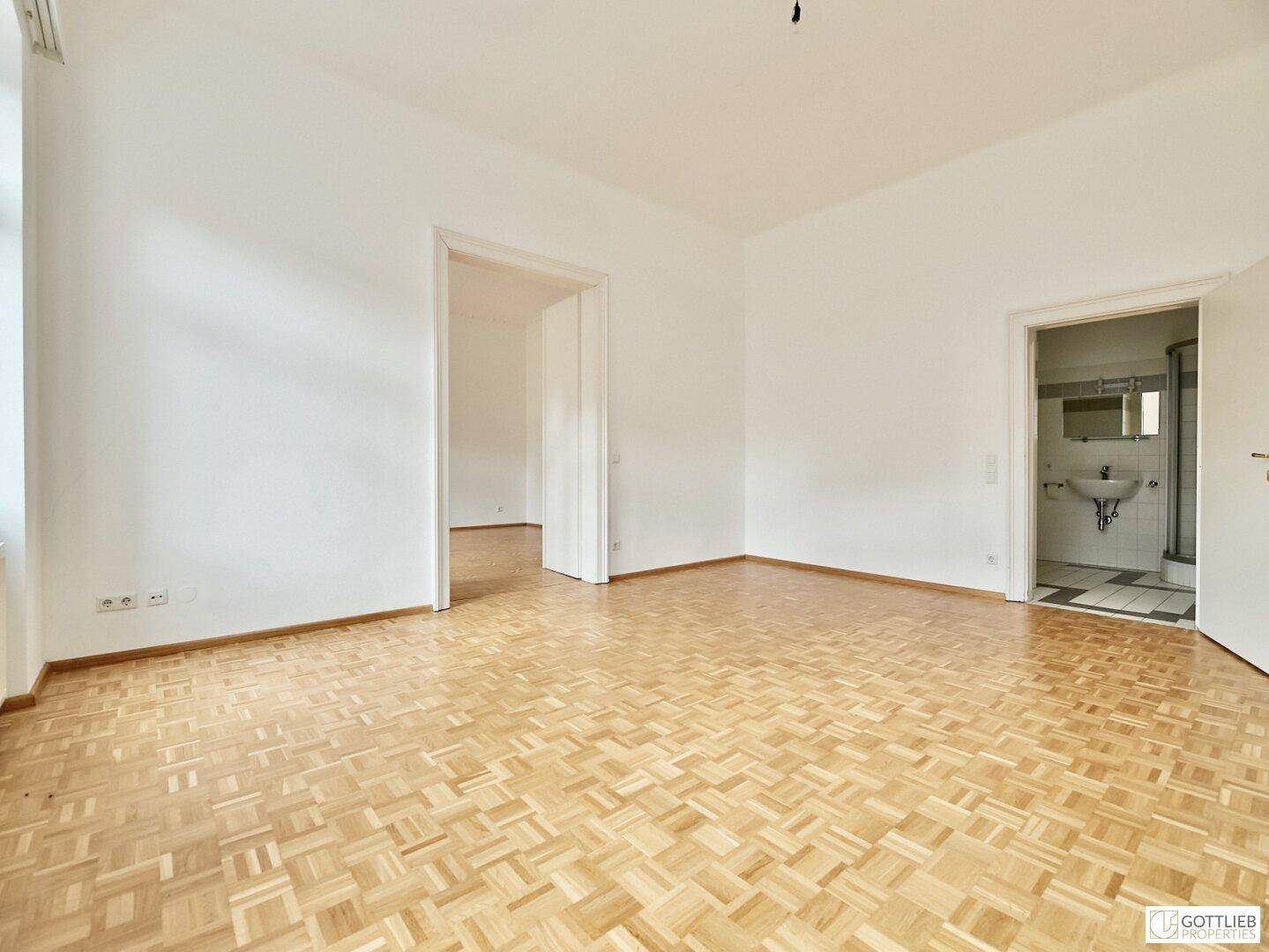 Großes, helles Zimmer mit Parkettboden und Zugang zu einem Badezimmer, ideal als Schlafzimmer.