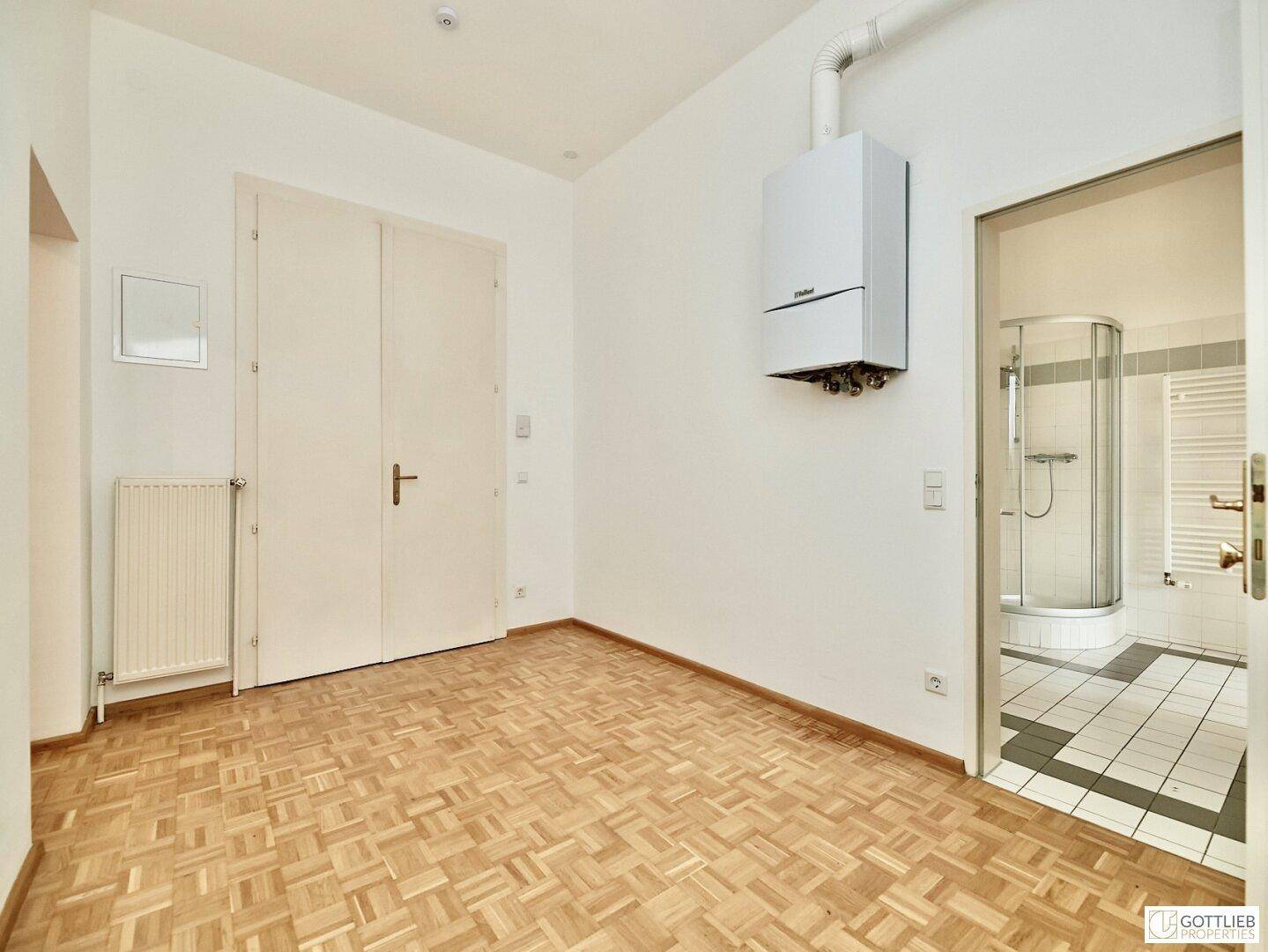 Helles Zimmer mit Parkettboden, Wandheizkessel und direktem Zugang zu einem Duschbad.