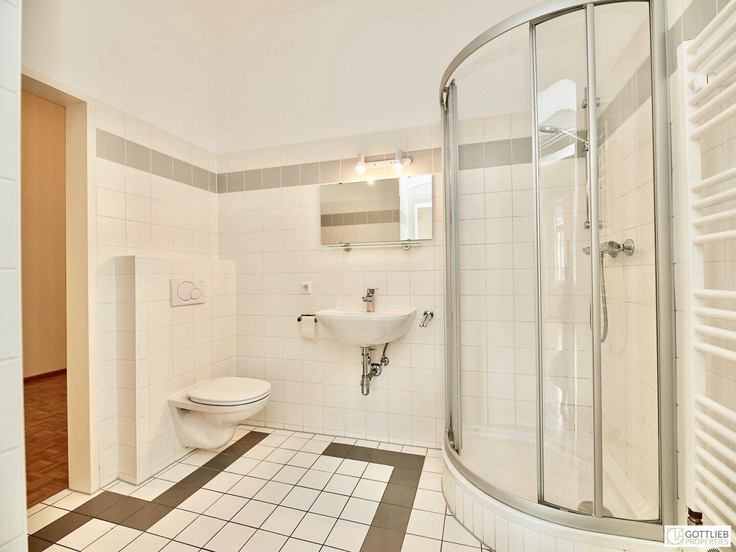 Modernes Badezimmer mit weiß-grauen Fliesen, Dusche, WC und Handtuchheizkörper.